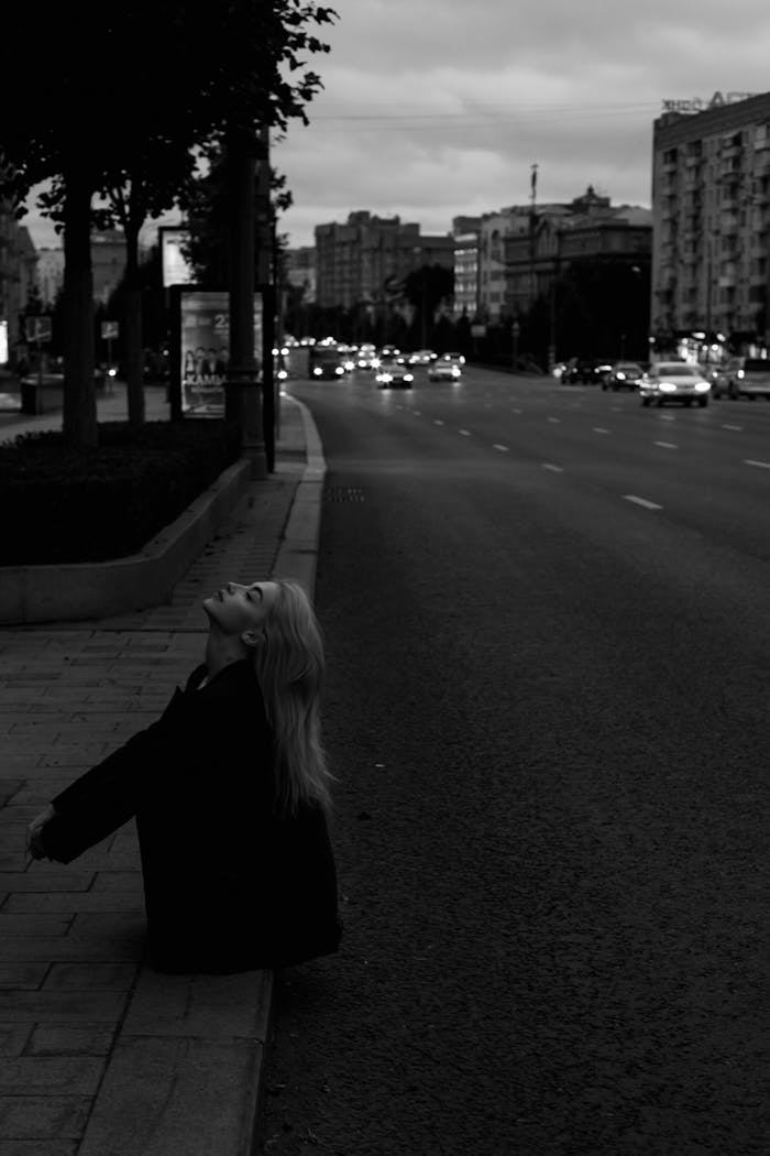 Black and white urban portrait of a woman on a city street at dusk, conveying a sense of solitude.