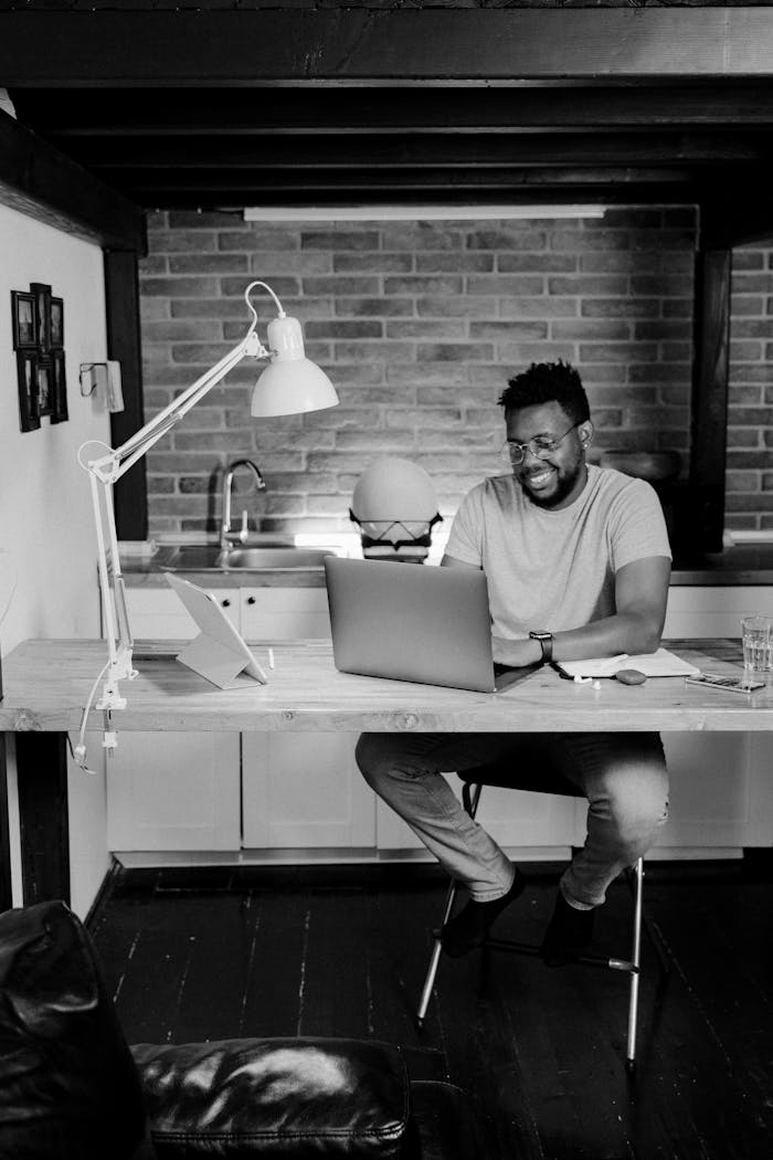 Black and white photo of an African American man working remotely at home from a laptop.
