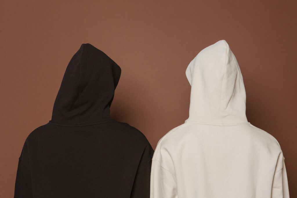 Back view of two hoodies in white and black against a brown background.